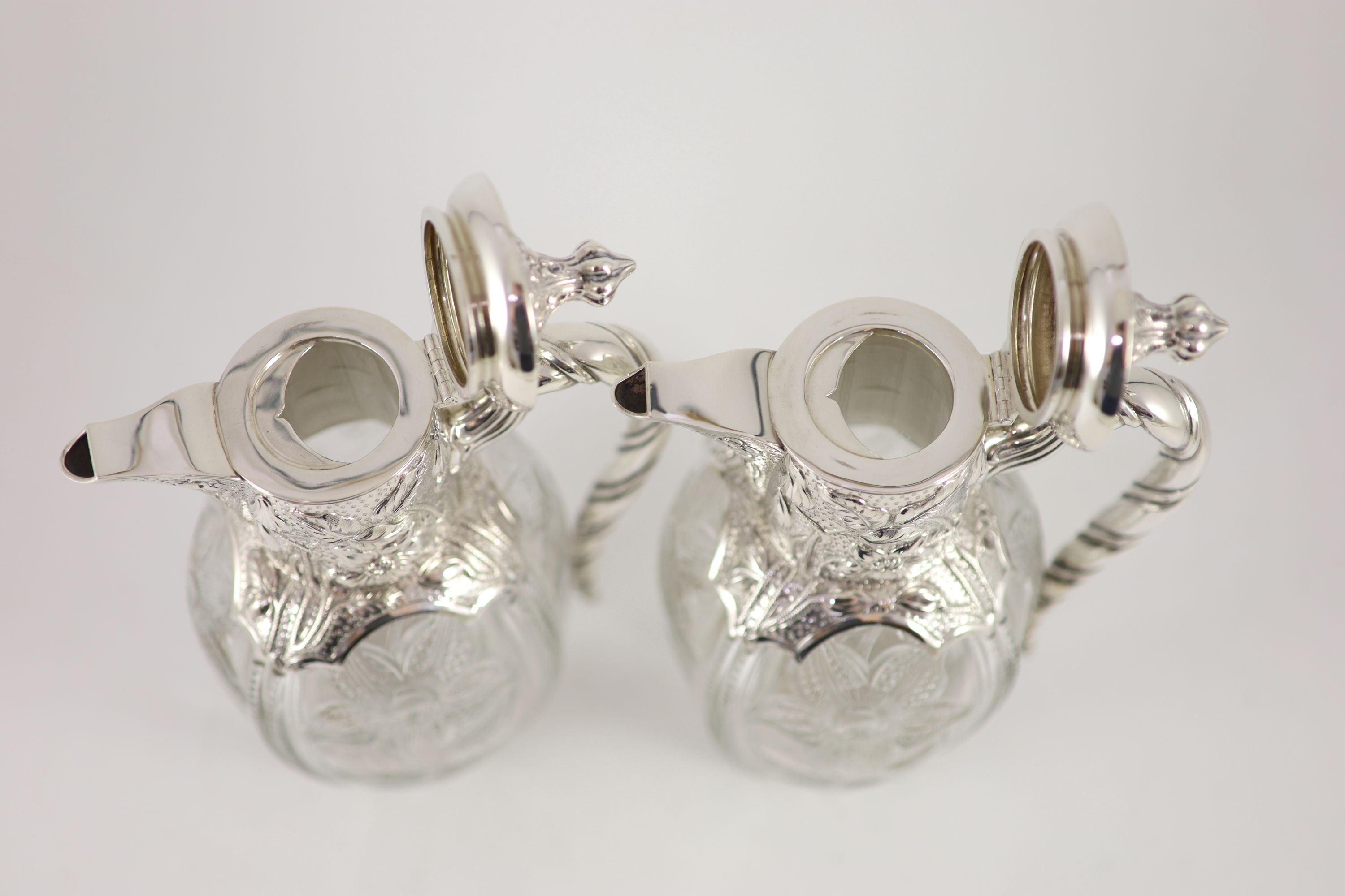 A good pair of late Victorian silver mounted ‘rock crystal’ glass claret jugs, with hinged covers, by John Grinsell & Sons